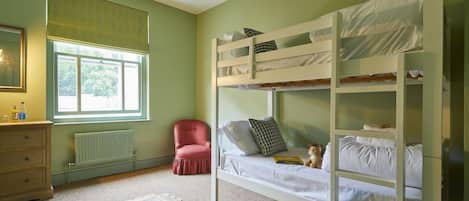 A bunk bed room with a window, a radiator, a chair, and a bedside table.