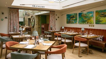 Un interior de restaurante con mesas de madera, sillas con cojines y un área de asientos central.