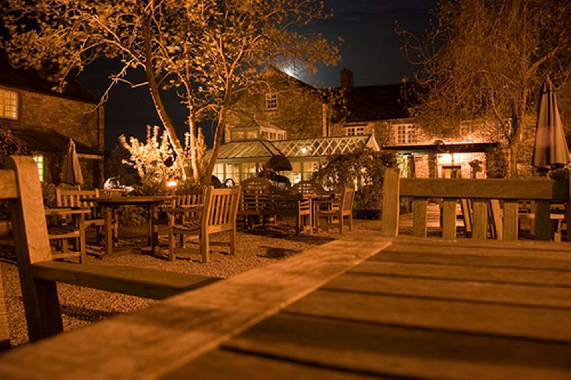 Ein Sitzbereich im Freien mit Tischen und Stühlen, eine Holzterrasse und ein Gebäude im Hintergrund.