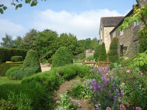 Un jardin bien entretenu, agrémenté d’un bâtiment en pierre, de haies taillées avec soin et de plantes en fleurs.