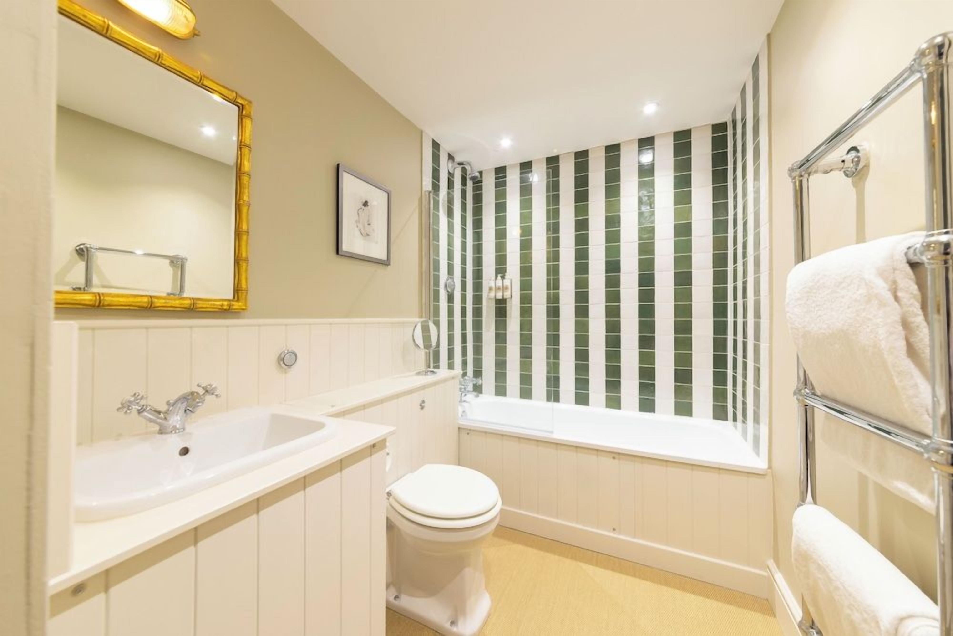 A bathroom with a white sink, a toilet, a bathtub, and a shower with green tiles.