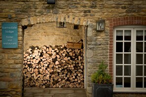 Un mur de pierres avec une enseigne indiquant « Barnsdale Lodge Hotel and Restaurant », une pile de bois de chauffage et une fenêtre ornée d’une plante à l’extérieur.