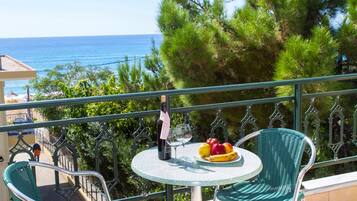 Ein Balkon mit Tisch, Stühlen, einer Weinflasche und einer Obstschale.