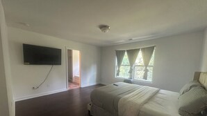 Un dormitori amb llit, televisió penjada a la paret i finestra amb cortines.