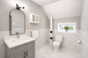 Un baño con lavamanos blanco, espejo, inodoro y ventana con una planta.