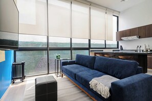 A modern kitchen with a large window, a blue sofa, and a small side table with decorative items. - w* | Deluxe 1BR in Escandón w/ Private Terrace (Ciudad de México)