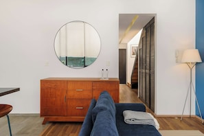 A modern hotel room with a wooden cabinet, a round mirror, a bed with a blue blanket, a floor lamp, and a view of a balcony. - w* | Deluxe 1BR in Escandón w/ Private Terrace (Ciudad de México)