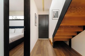 A narrow hallway with a bed on the left, a door in the center, and a wooden staircase on the right. - w* | Deluxe 1BR in Escandón w/ Private Terrace (Ciudad de México)