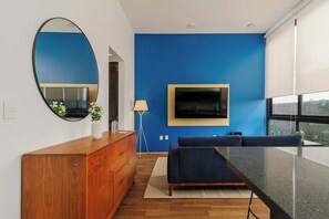 A modern living room with a blue accent wall, a large flat-screen TV, a wooden dresser, a blue sofa, and a floor lamp. - w* | Deluxe 1BR in Escandón w/ Private Terrace (Ciudad de México)
