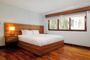 A modern bedroom with a wooden headboard, a large bed, a bedside table with a lamp, and a window with a view of greenery. - w* | Luxury & Cozy 1BR in Prime Polanco (Ciudad de México)