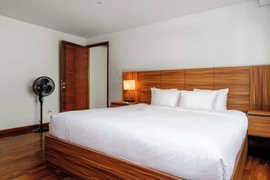A hotel room with a wooden bed frame, white bedding, a bedside table with a lamp, and a standing fan. - w* | Luxury & Cozy 1BR in Prime Polanco (Ciudad de México)