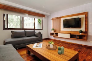 A modern living room with a sofa, a coffee table with decorative items, a television mounted on the wall, and large windows. - w* | Luxury & Cozy 1BR in Prime Polanco (Ciudad de México)