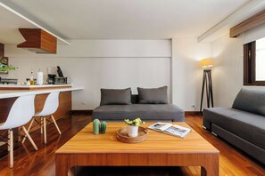 A modern living room with a grey sofa, a wooden coffee table, and a kitchen area with white chairs and appliances. - w* | Luxury & Cozy 1BR in Prime Polanco (Ciudad de México)