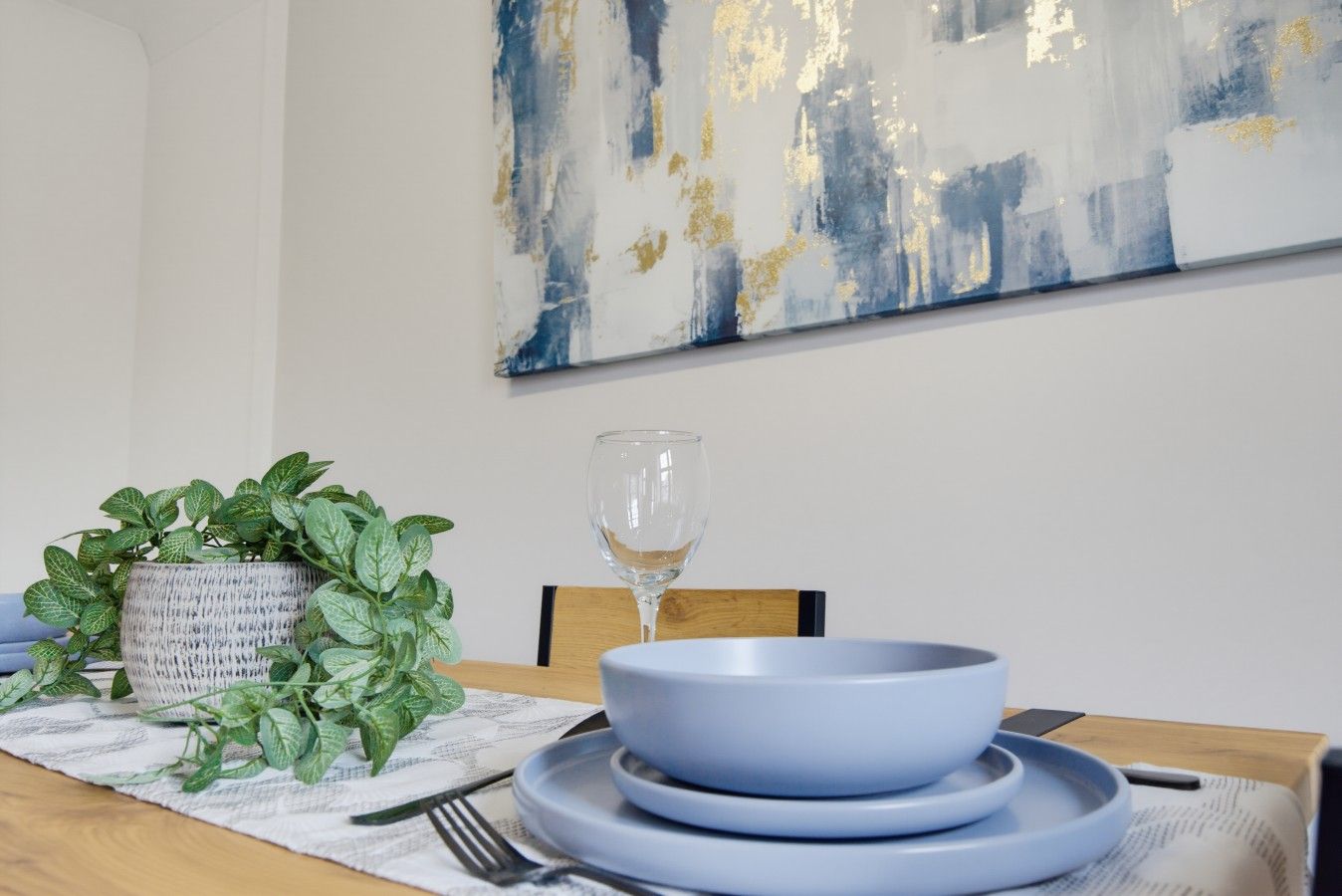 Una mesa de comedor con un tazón azul, un vaso, un tenedor, un cuchillo y una planta en maceta.