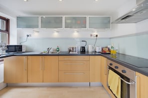 A modern kitchen with wooden cabinets, a microwave, a coffee maker, and a stove. - Family & Pet Friendly Flat | Free Parking&Wi-fi (Ceredigion)