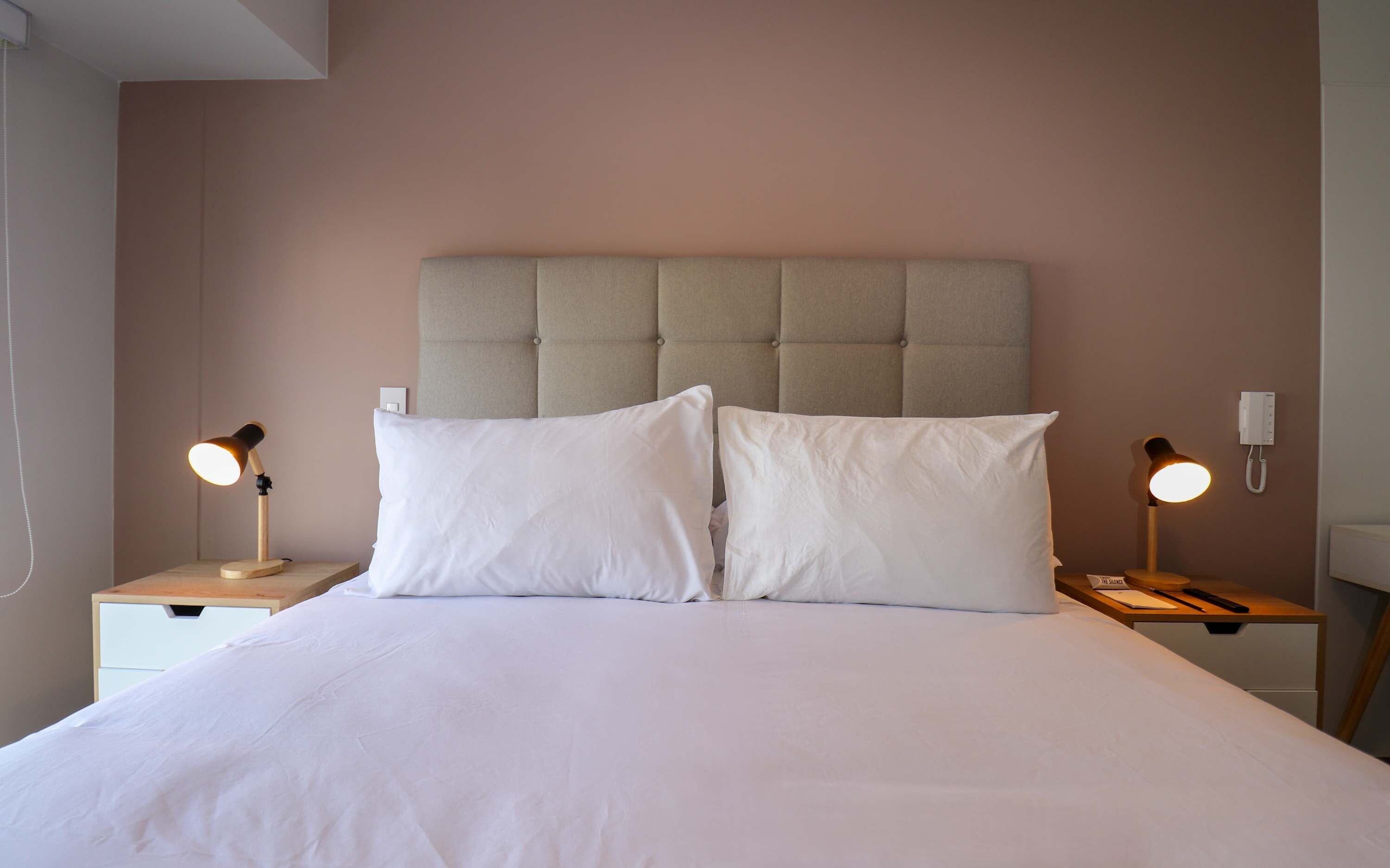 A bed with a tufted headboard, two bedside tables with lamps, and a wall-mounted phone.