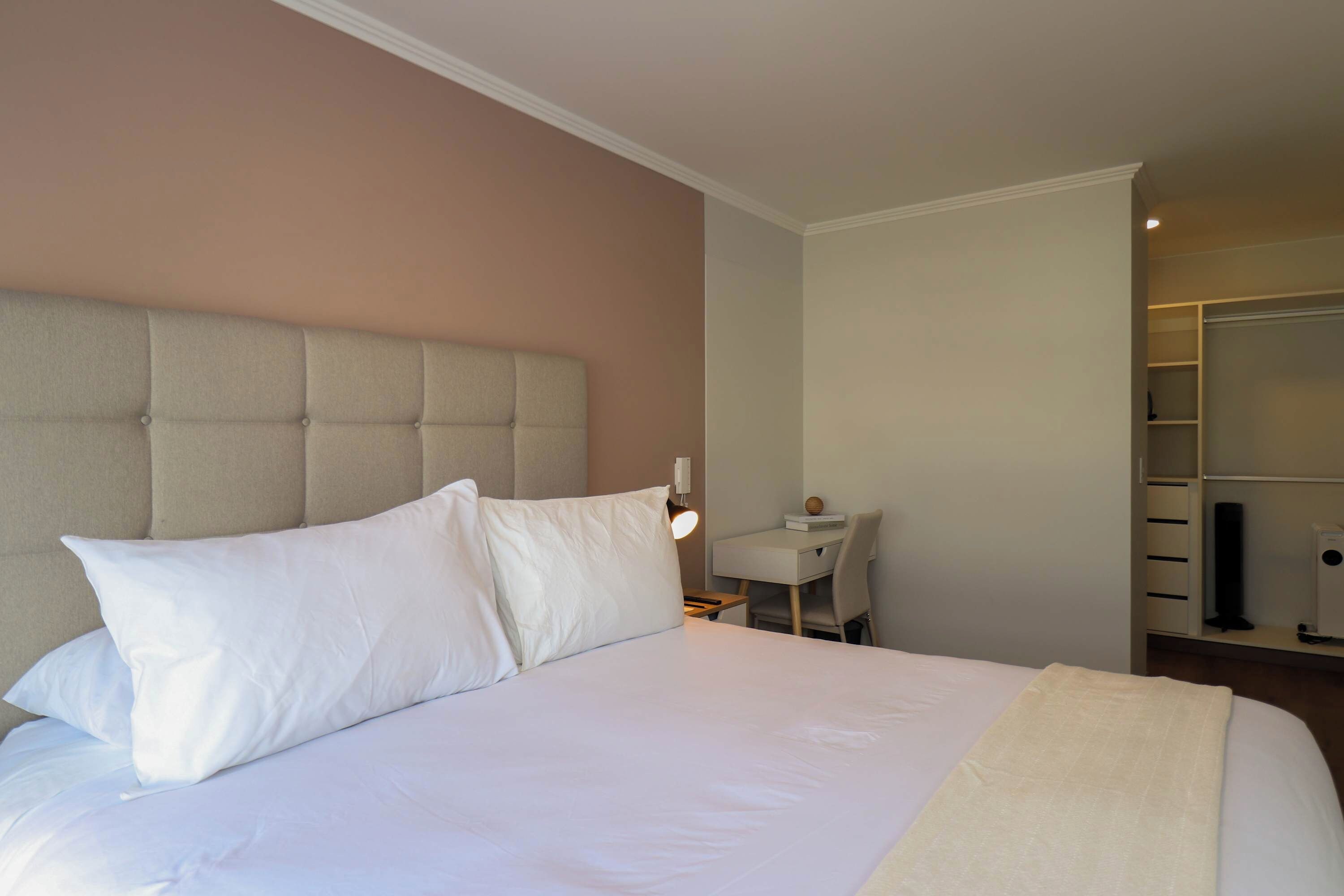 A hotel room with a large bed, a bedside table, a desk, and a wardrobe.
