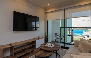 Ein modernes Wohnzimmer mit Fernseher, einer hölzernen Bank, einem runden Couchtisch und einer Couch.