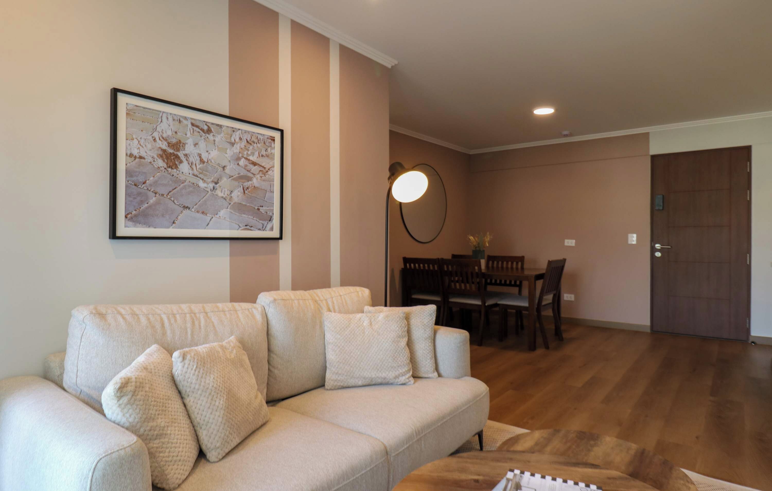 A living room with a sofa, a dining table with chairs, a wall-mounted lamp, and a framed picture.