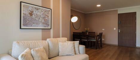 A living room with a sofa, a dining table with chairs, a wall-mounted lamp, and a framed picture.