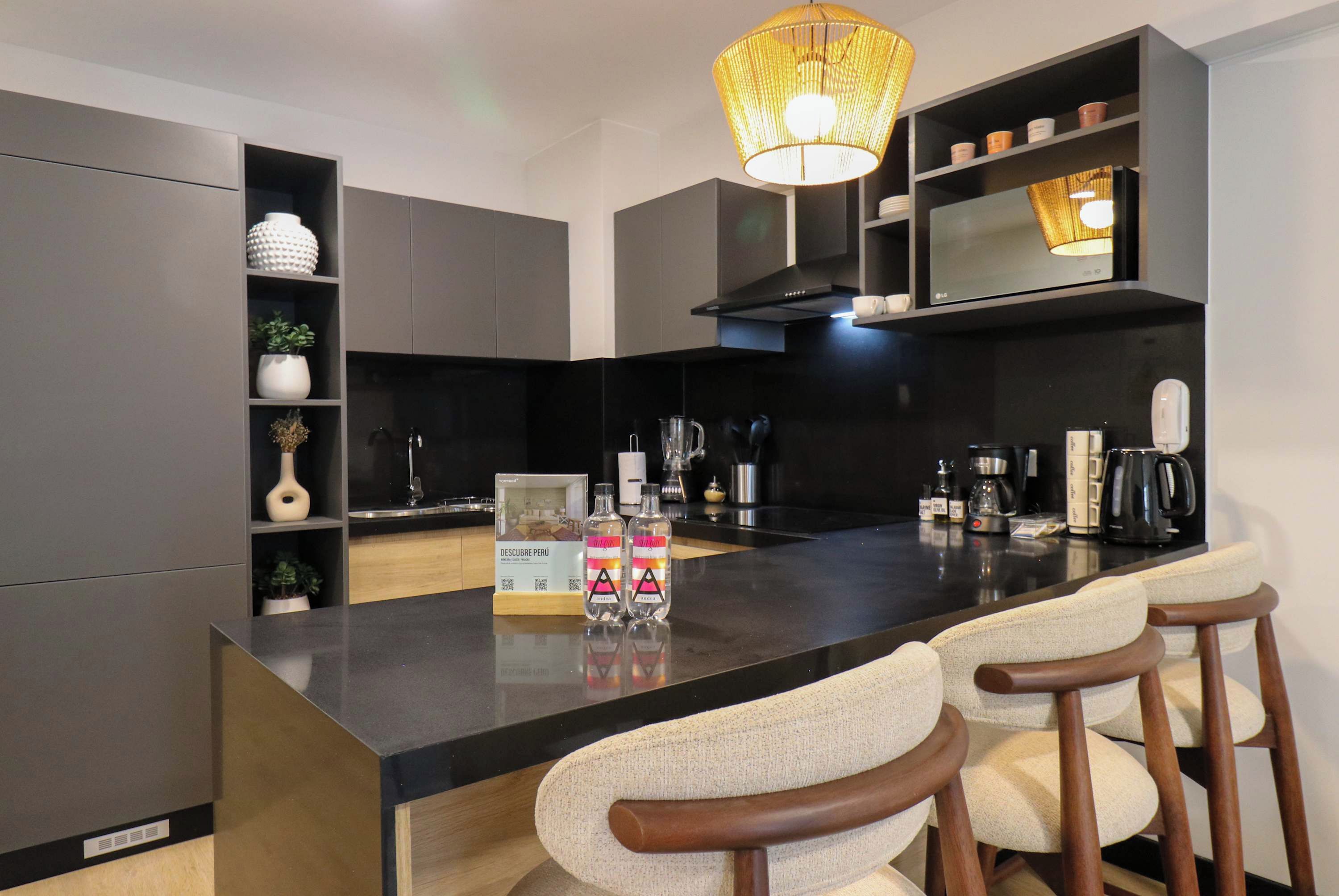 A modern kitchen with a central island, bar stools, a hanging light fixture, and a coffee machine.