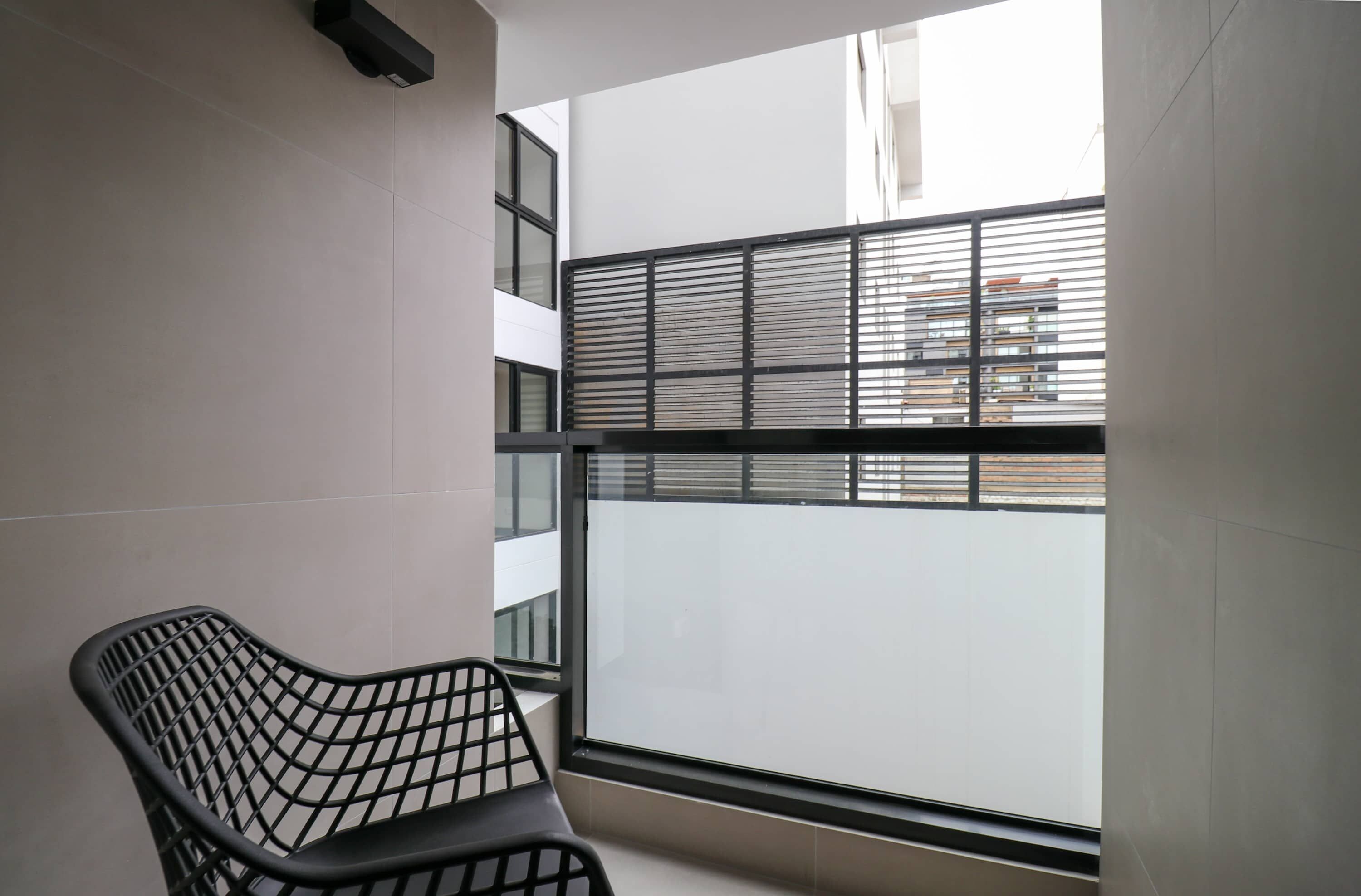 A modern room with a black metal chair, a window with horizontal blinds, and a view of a building outside.
