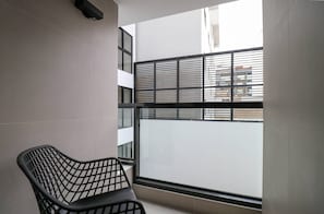 A modern room with a black metal chair, a window with horizontal blinds, and a view of a building outside. - w* | Modern 2BR w/ Balcony in Prime Miraflores (Miraflores)
