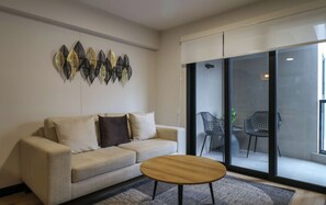A living room with a sofa, a coffee table, and a view through a glass door to an outdoor seating area. - w* | Modern 2BR w/ Balcony in Prime Miraflores (Miraflores)