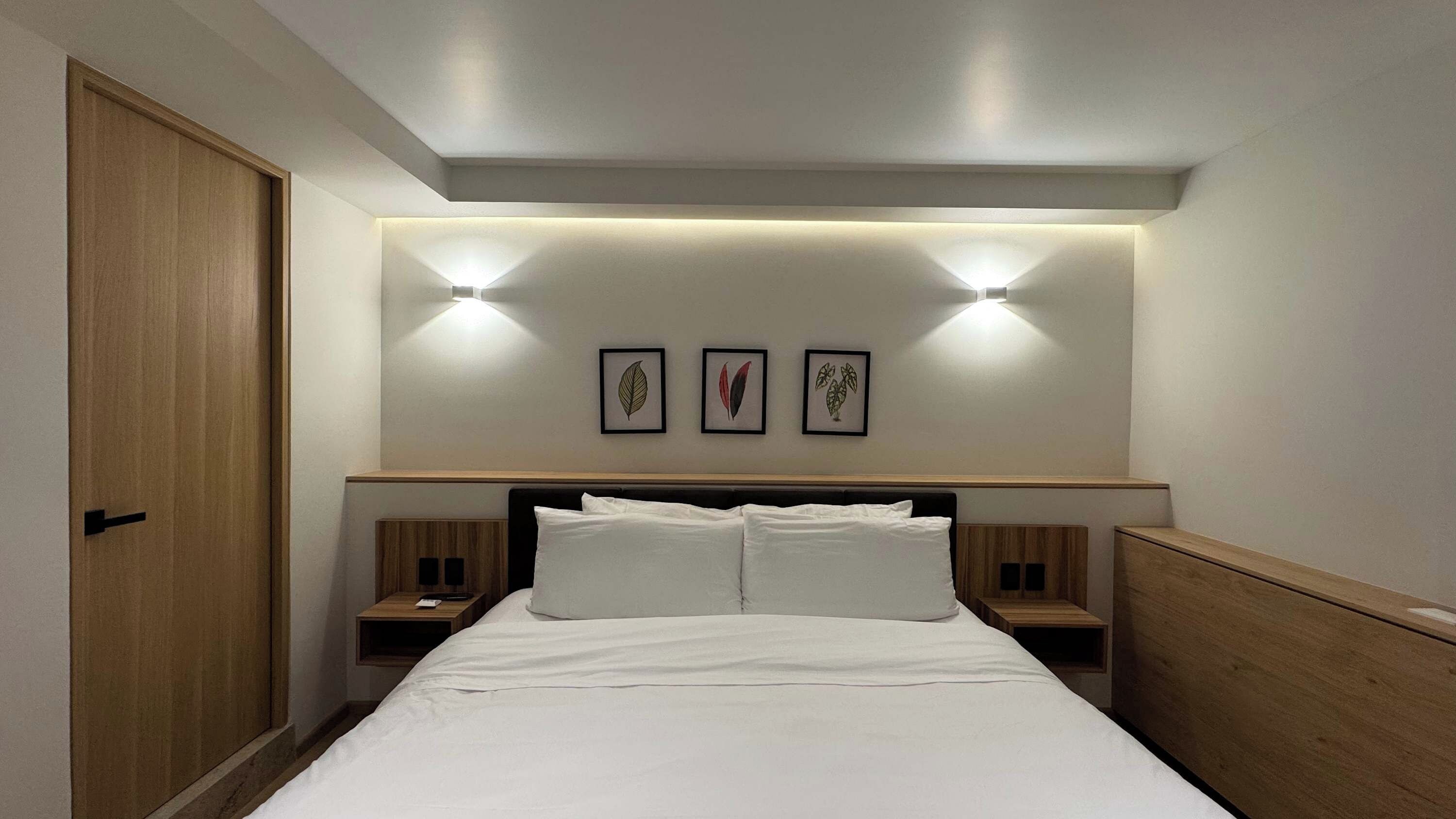 A hotel room with a bed, two bedside tables, and a headboard with wall-mounted lights.