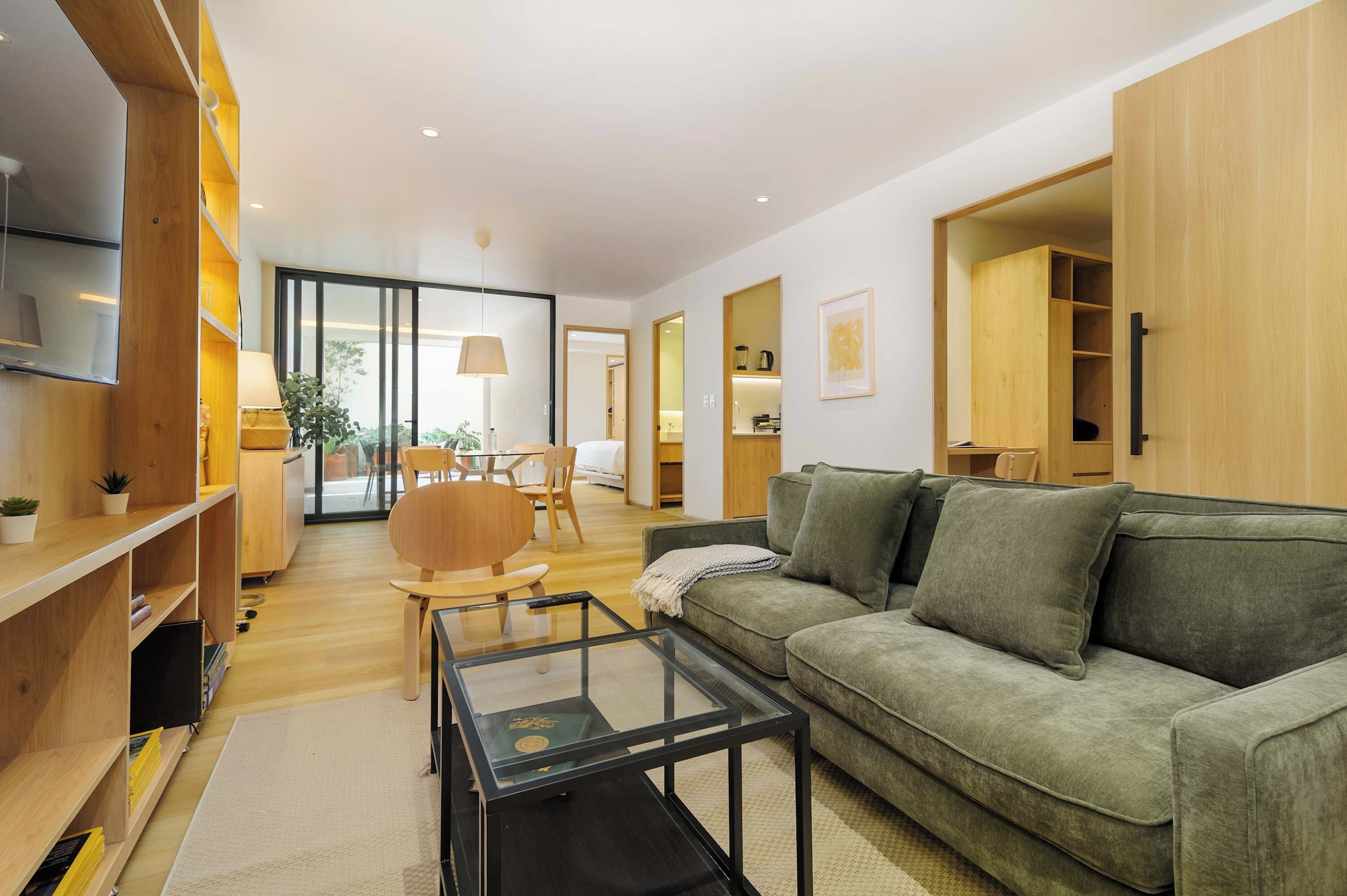 A modern living room with a green sofa, a glass coffee table, and wooden shelving.