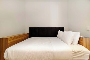 Ein Hotelzimmer mit Bett, Holz-Kopfschild, weißer Bettwäsche und einem Nachttisch mit Lampe.