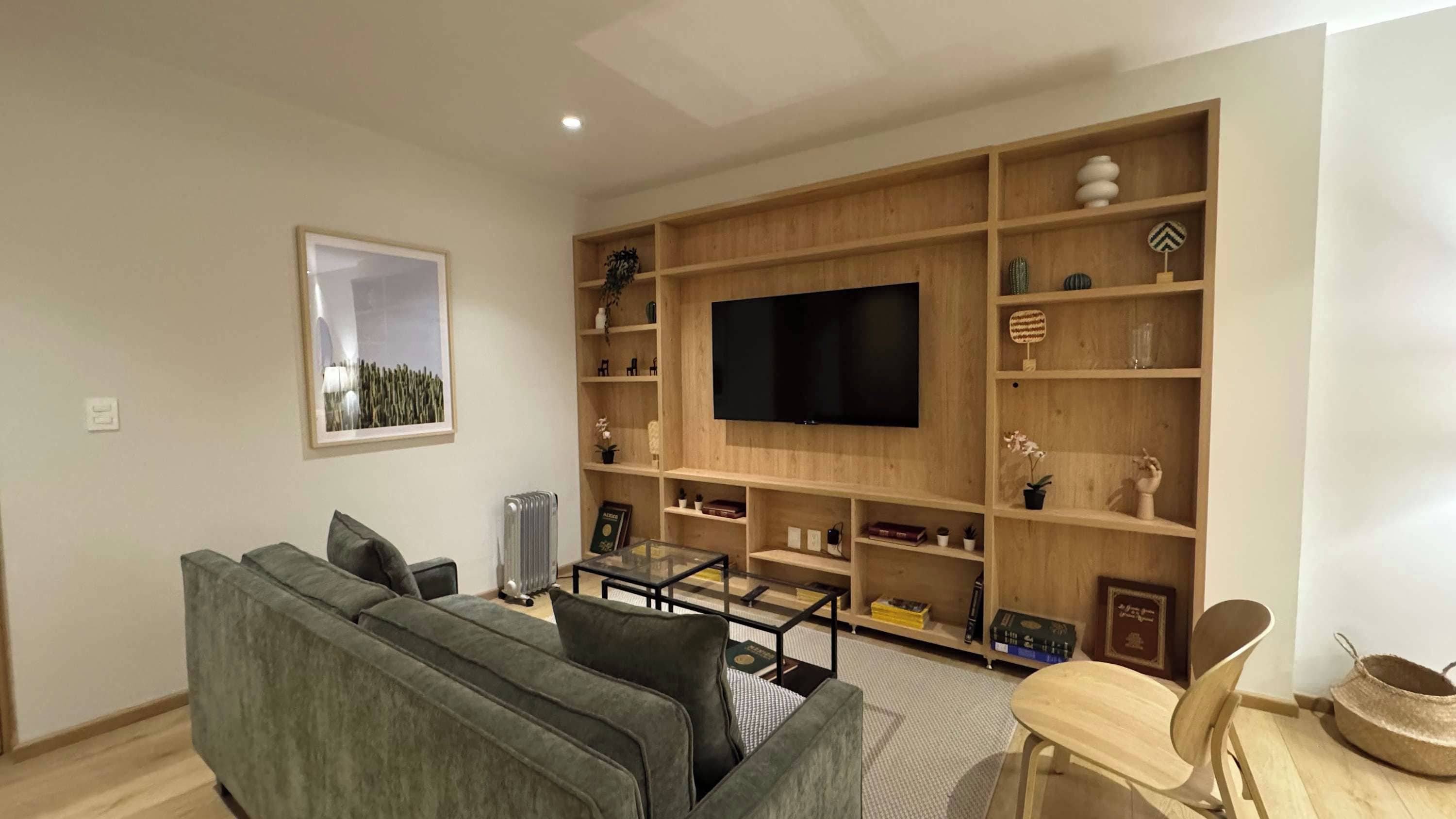 A modern living room with a grey sofa, a coffee table, a TV mounted on a wooden wall, and shelves with various decorative items.