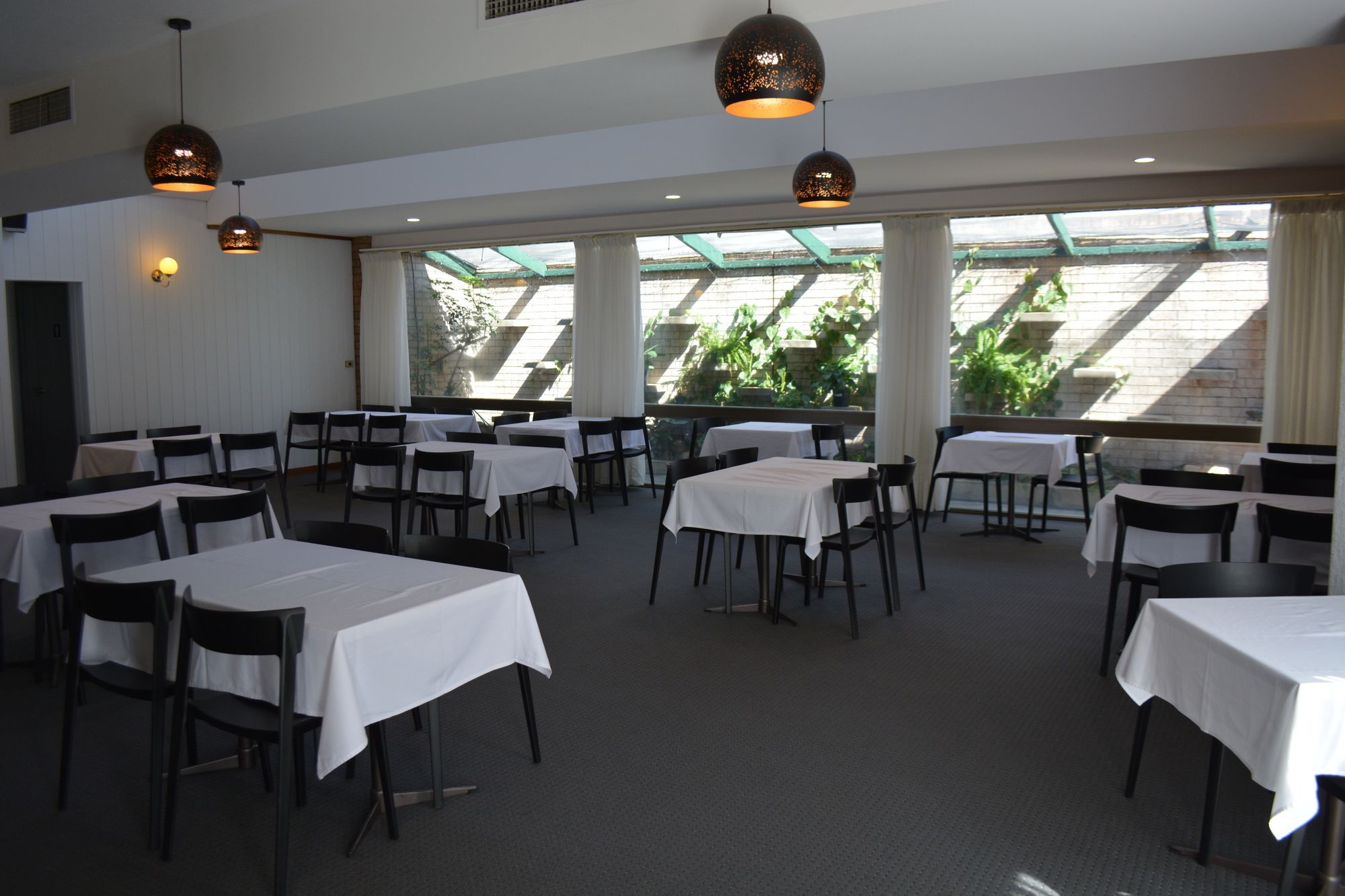 A dining area with tables and chairs, large windows, and hanging pendant lights.