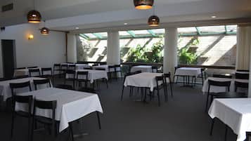 A dining area with tables and chairs, large windows, and hanging pendant lights.