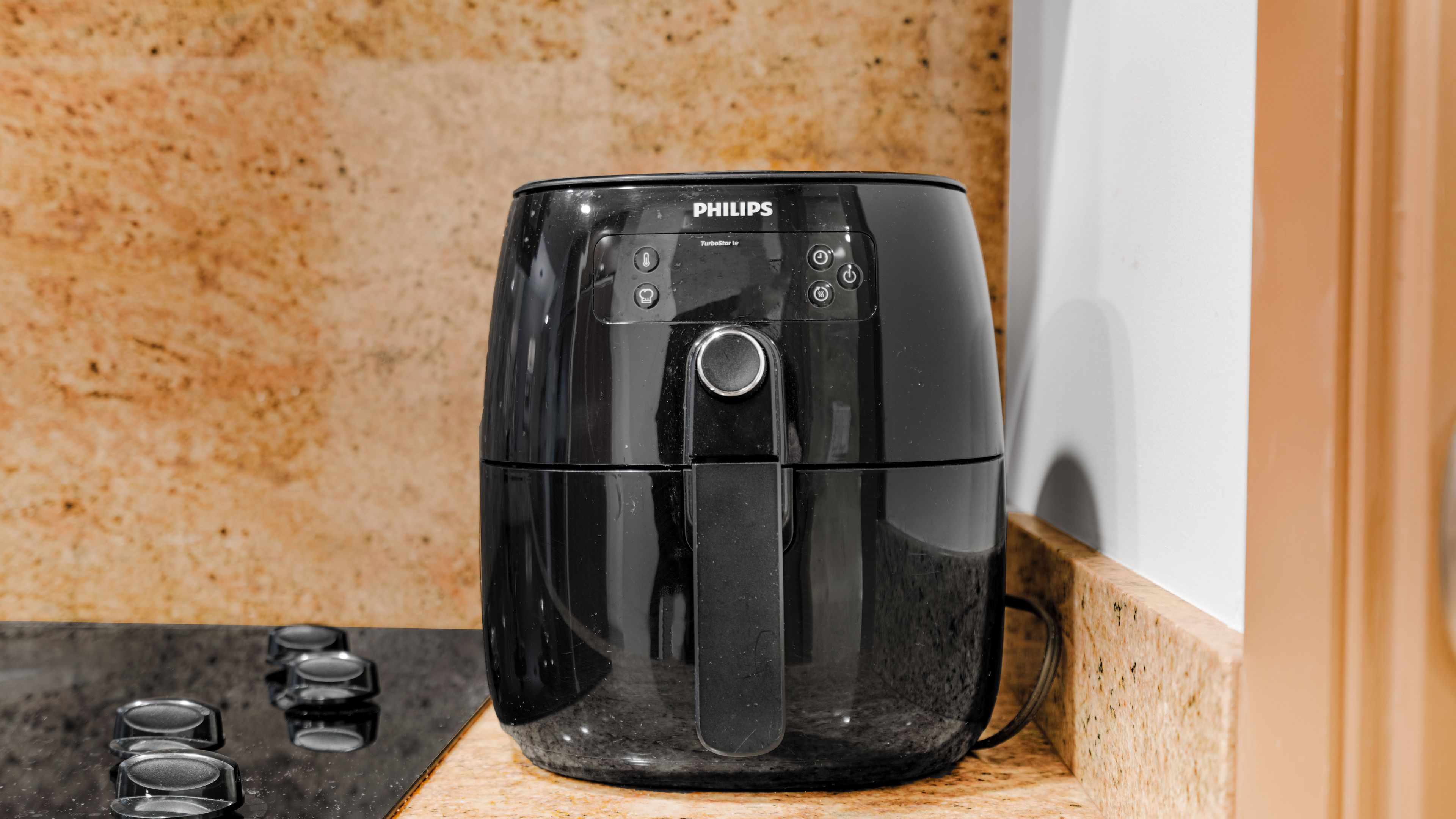 Una freidora de aire Philips TurboStar sobre una encimera de cocina con cubierta de granito y un armario de madera.