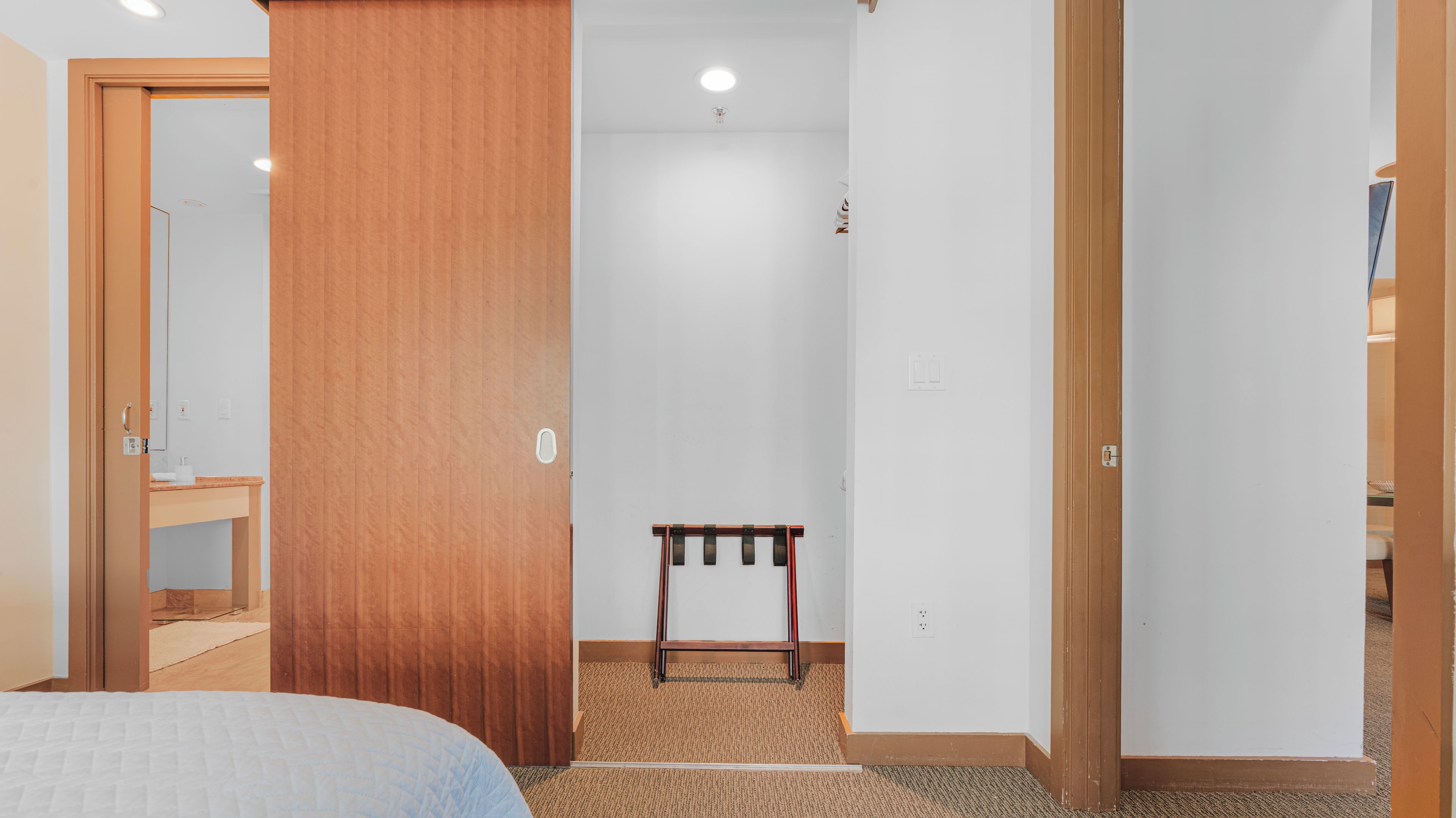 A hotel room with a bed, a wooden wardrobe, a small table, and a carpeted floor.