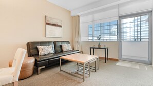 A modern living room with a leather sofa, a wooden coffee table, and a large window with a city view.