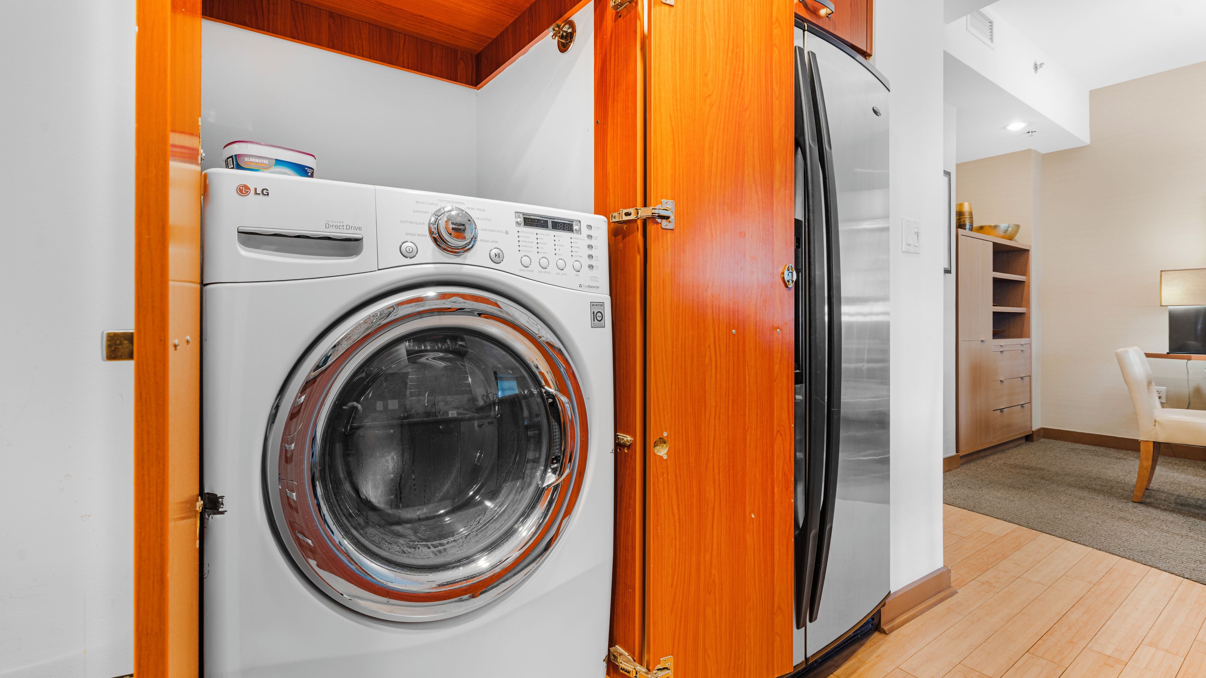 Une petite buanderie comprenant un lave-linge, un réfrigérateur, des placards en bois et un petit coin salon.