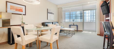 Ein modernes Wohnzimmer mit einem Glastisch, Ledersofas, einem Flachbildfernseher und einem großen Fenster mit Blick auf die Stadt.