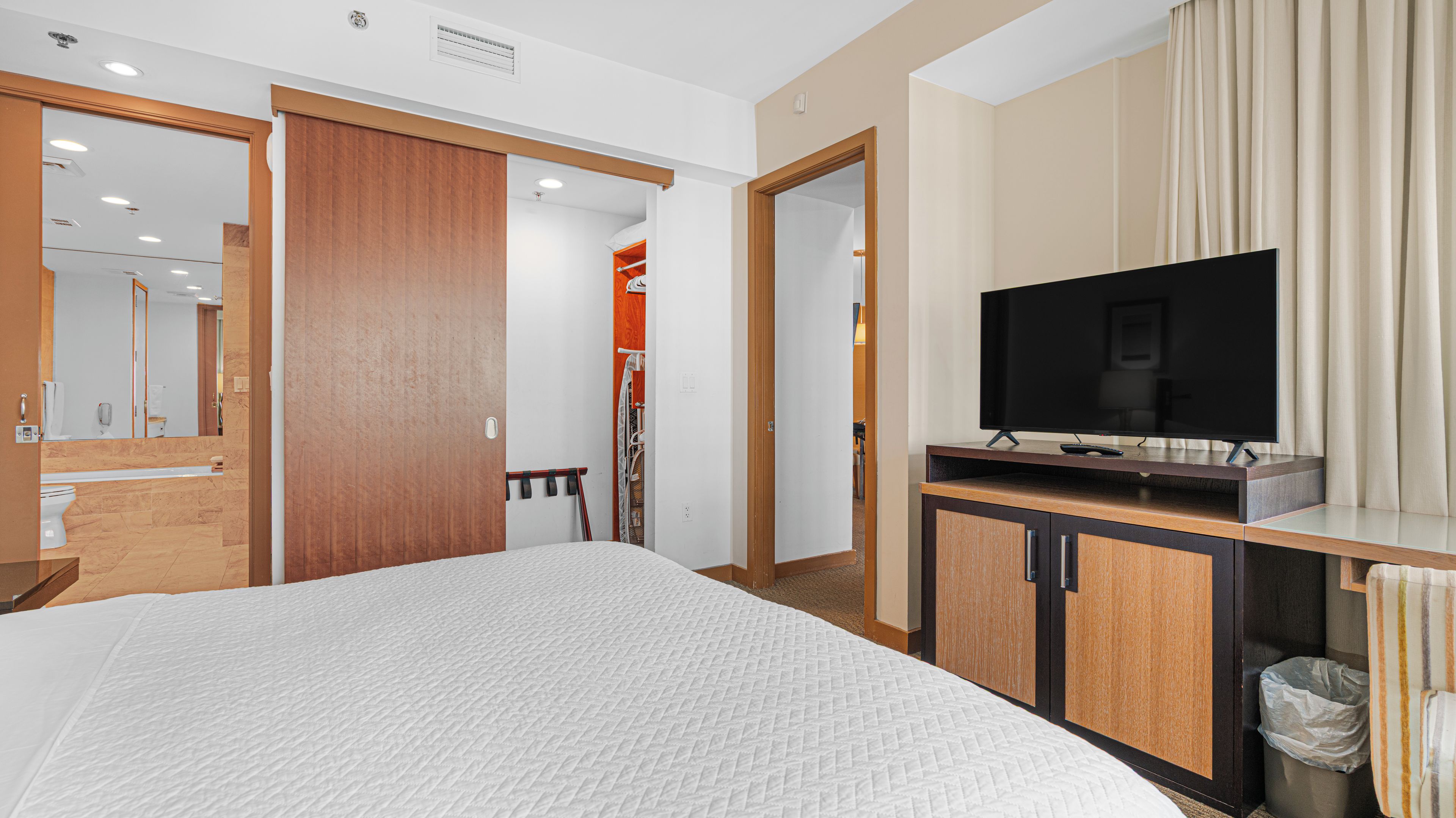 Une chambre d’hôtel avec un lit, une télévision, une armoire et une salle de bain, visibles à travers une porte ouverte.
