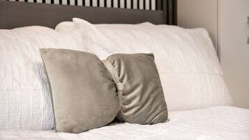 Una cama con ropa de cama blanca y dos almohadas color beige.