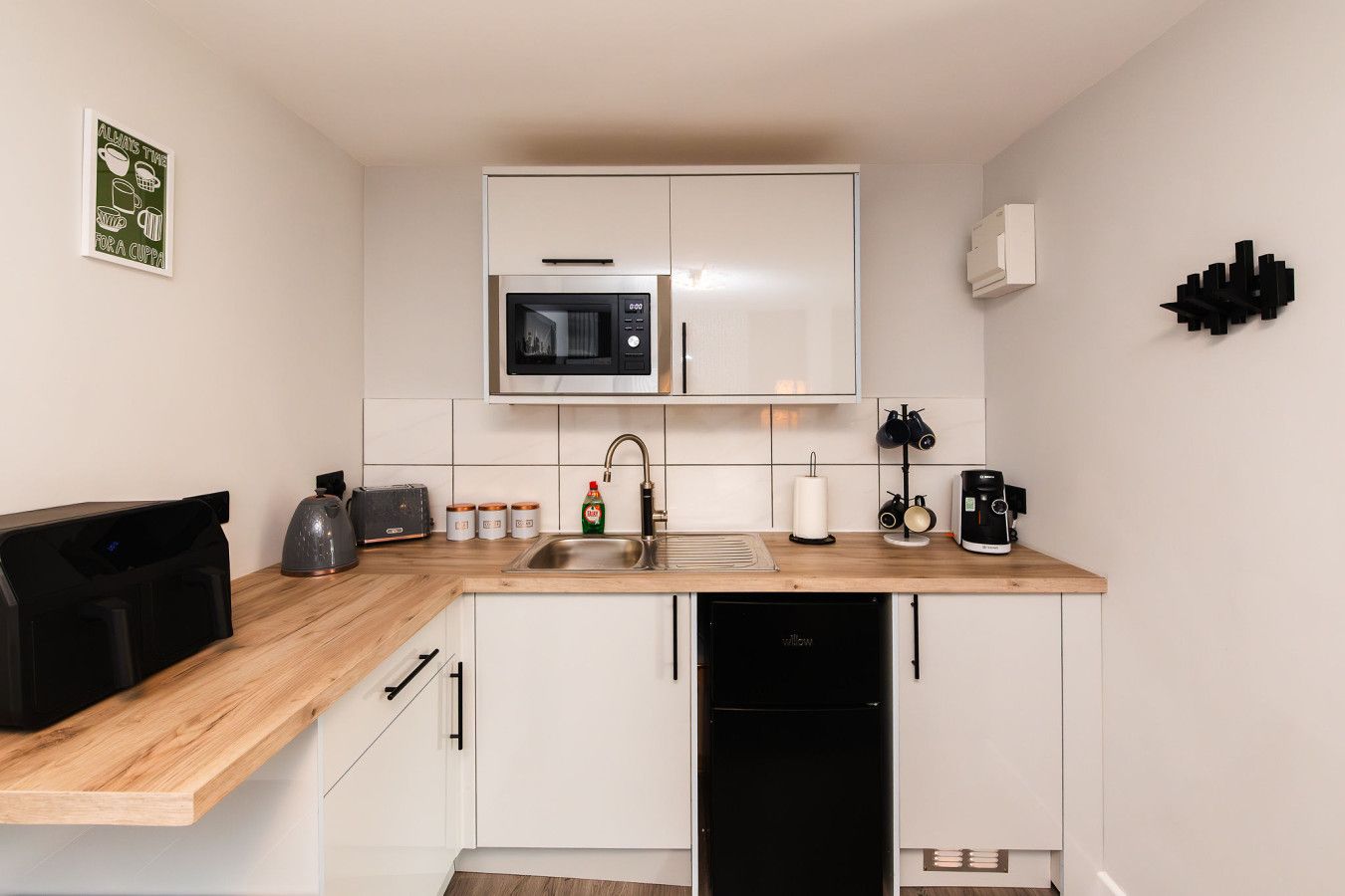 Een praktische keuken met een magnetron, broodrooster, spoelbak en koffiezetapparaat.