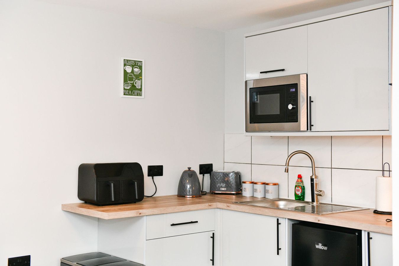 A modern kitchen with white cabinets, a microwave, a kettle, a toaster, and a dishwasher.