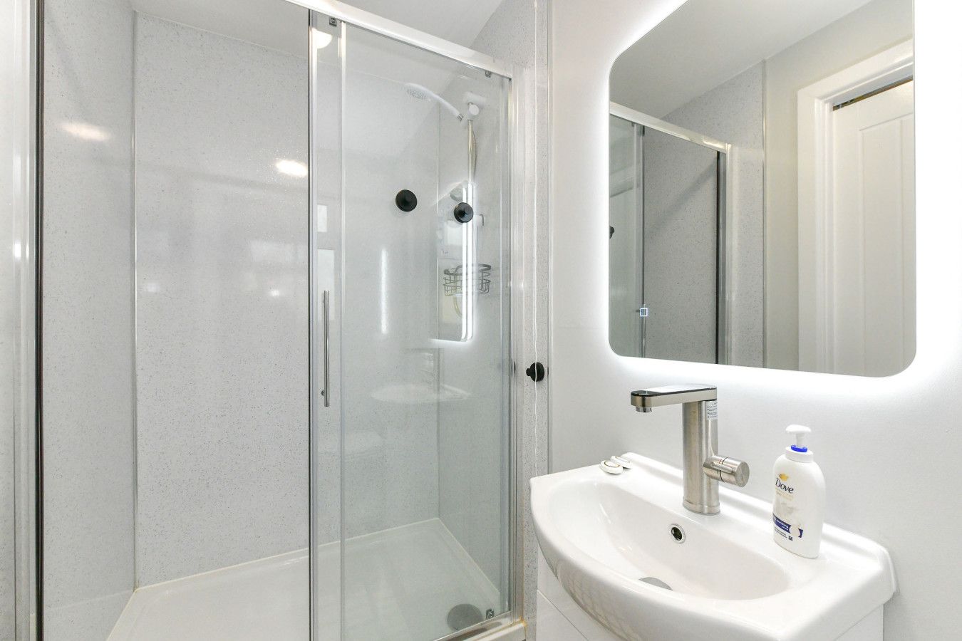 Un baño moderno con ducha de vidrio, lavamanos blanco y espejo.