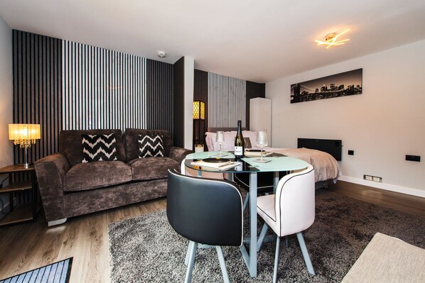 Un salon moderne avec un canapé, une table à manger et des chaises, une lampe et un tableau représentant un paysage urbain accroché au mur.