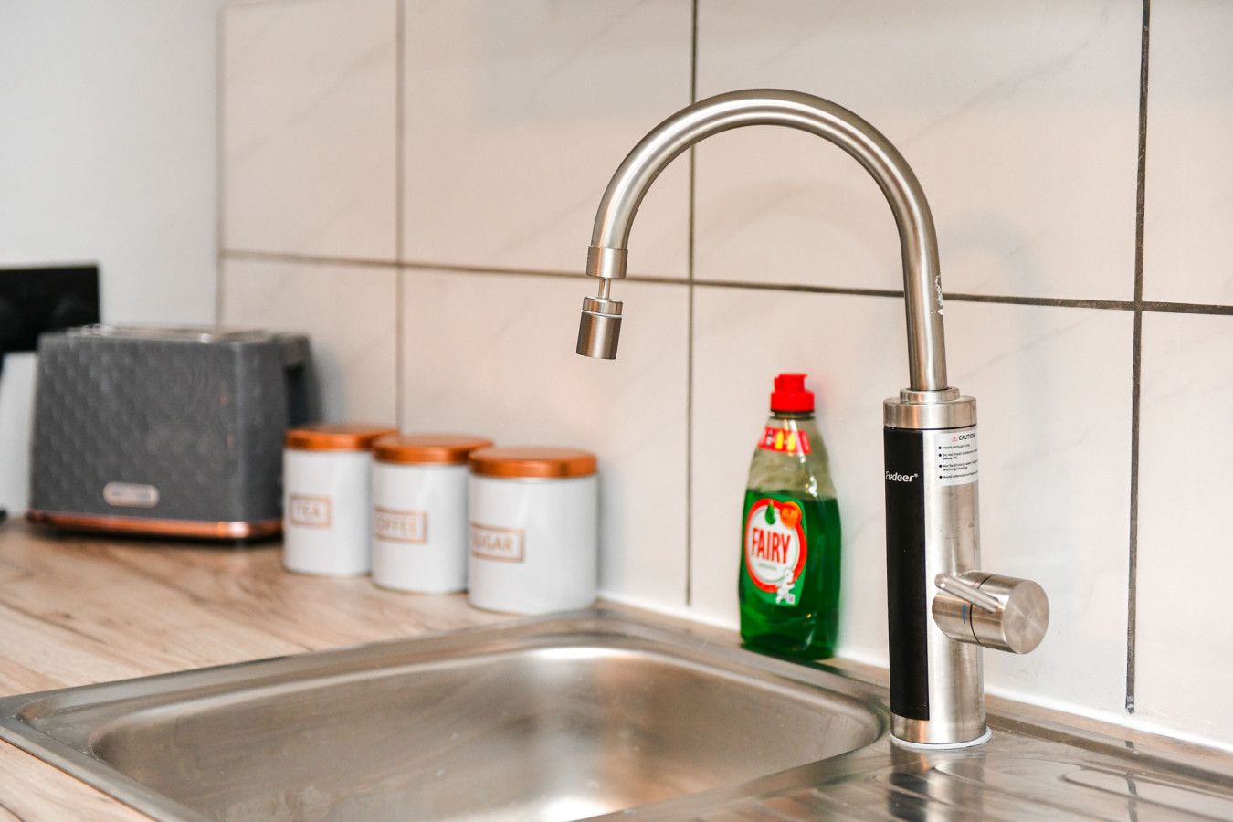A kitchen sink with a modern faucet, a bottle of Fairy dish soap, and three jars with orange lids.