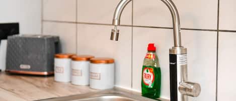 A kitchen sink with a modern faucet, a bottle of Fairy dish soap, and three jars with orange lids.