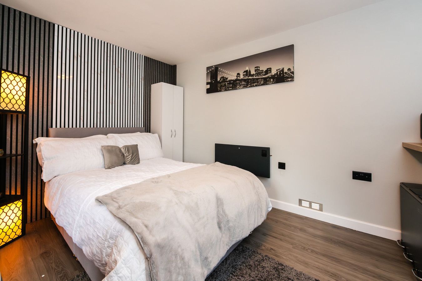 A modern bedroom with a bed, a wall-mounted TV, and a cityscape painting.