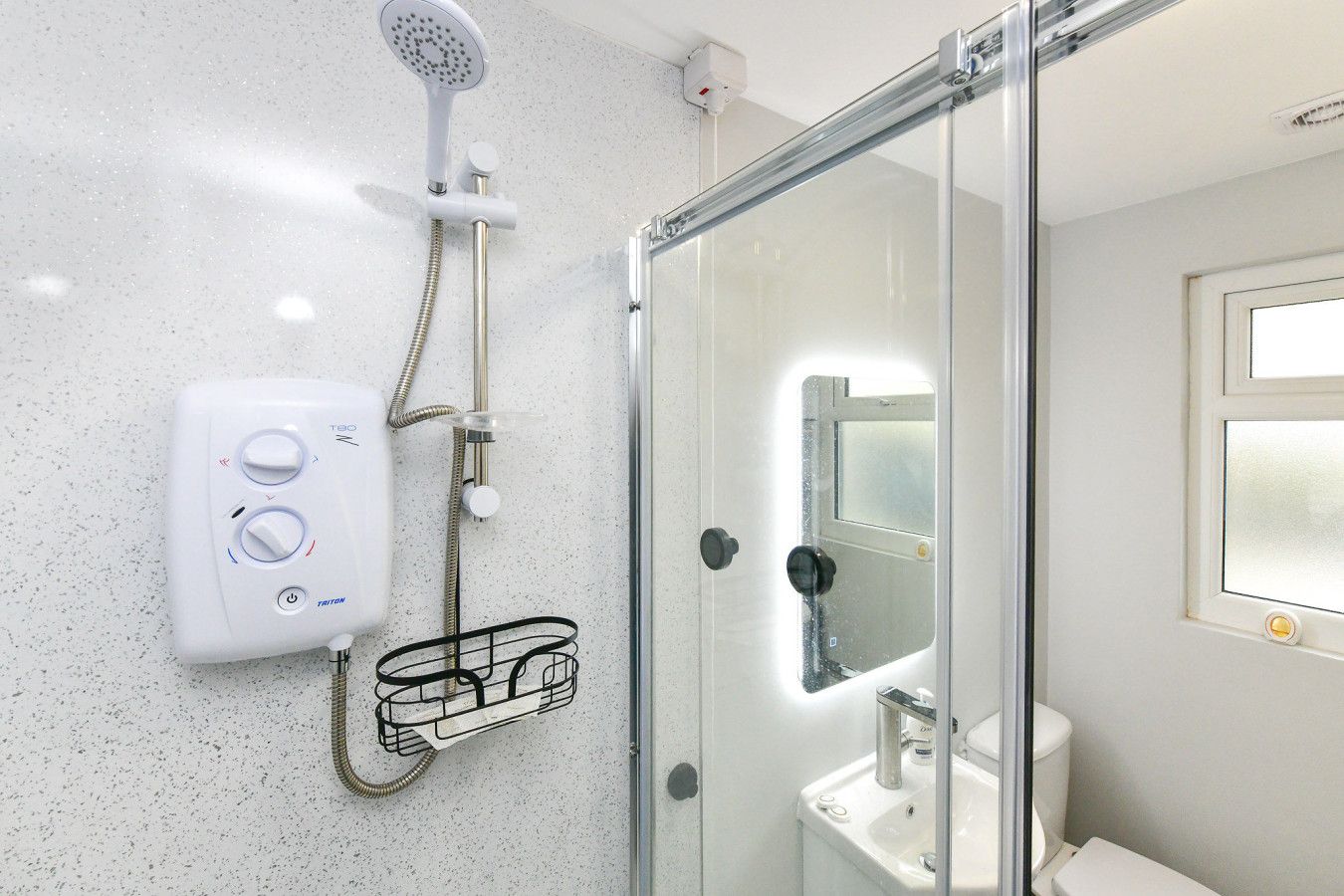 A modern bathroom with a glass shower enclosure, a handheld showerhead, a wall-mounted control panel, and a toilet.