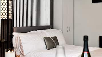 A hotel room with a bed, a bedside table with a candle, a bottle of wine, and a wall-mounted TV.